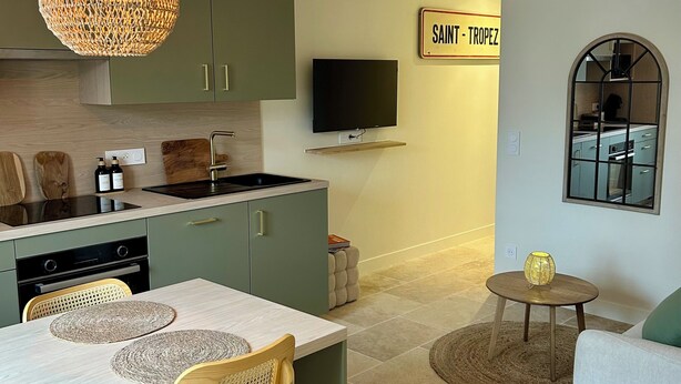 Een moderne keuken met een eethoek, een televisie en een bord met de tekst 'SAINT-TROPEZ'.