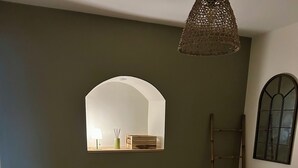 Een netjes opgemaakt bed met groene en witte kussens, een bedlampje en een geweven lamp boven het bed.