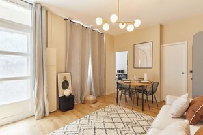 A modern living room with a dining area, large windows with curtains, a chandelier, and a framed artwork on the wall. - Bright Cosy Suite Paris 16th Steps from Seine (Paris)