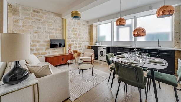 Ein modernes Wohnzimmer mit Steinwand, einer Couch, einem Couchtisch und einem Essbereich mit Stühlen und Tisch für zwei Personen.