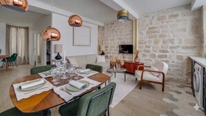 Ein modernes Wohnzimmer mit Steinwand, einer Essecke mit Holztisch gedeckt für vier Personen und einer Küchenzeile mit Waschmaschine.