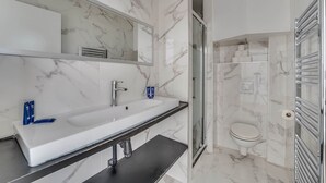 Ein Badezimmer mit weißem Waschbecken, Spiegel und Toilette, Marmorwänden und einer Duschkabine.