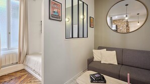 Un salon moderne avec un canapé, une table basse sur laquelle repose un livre, un miroir et une fenêtre avec des rideaux.