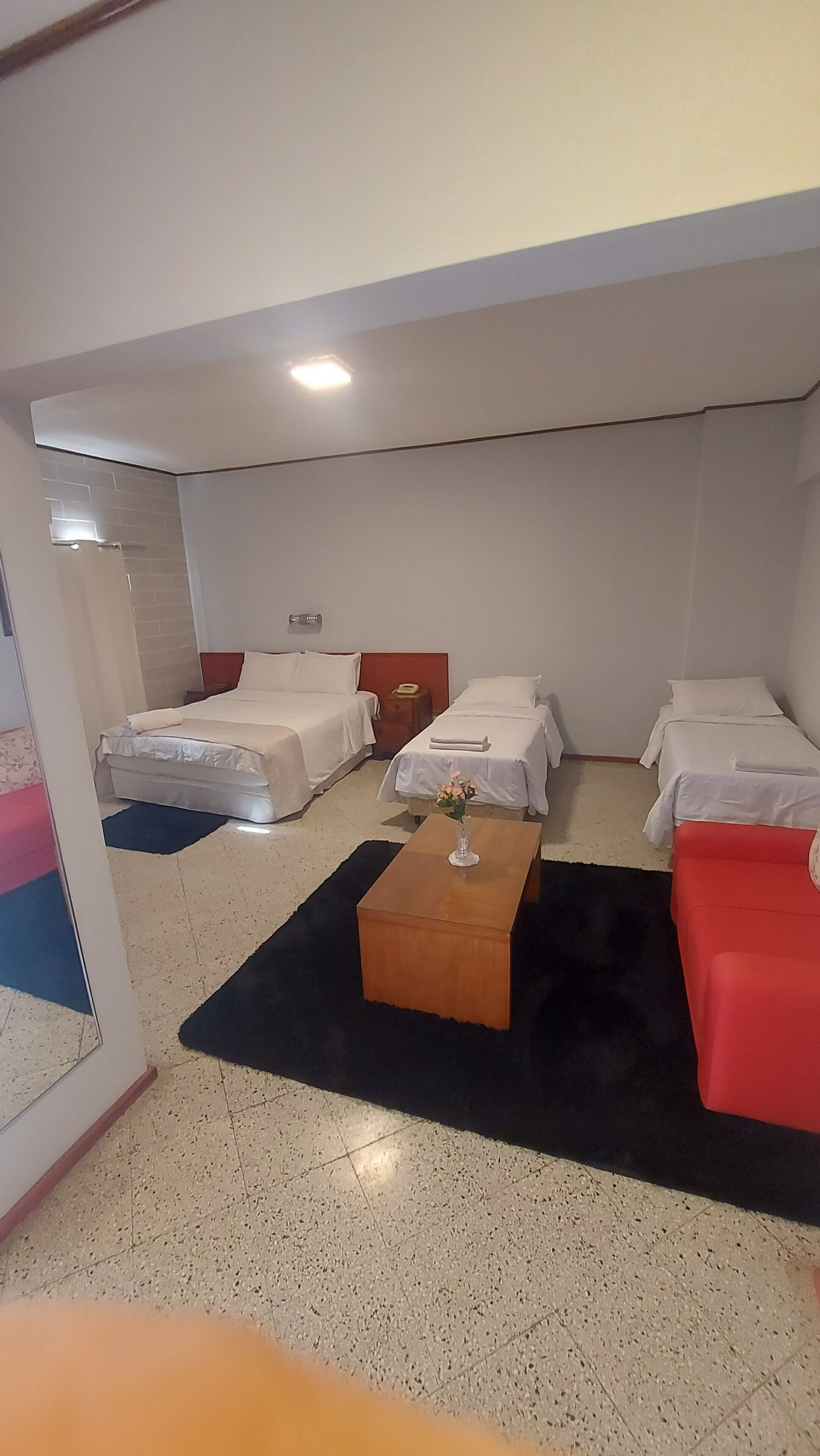 A hotel room with three beds, a wooden coffee table, and a red couch.
