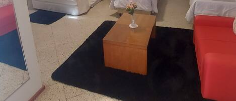 Ein Hotelzimmer mit drei Betten, einem Holztisch und einem roten Sofa.
