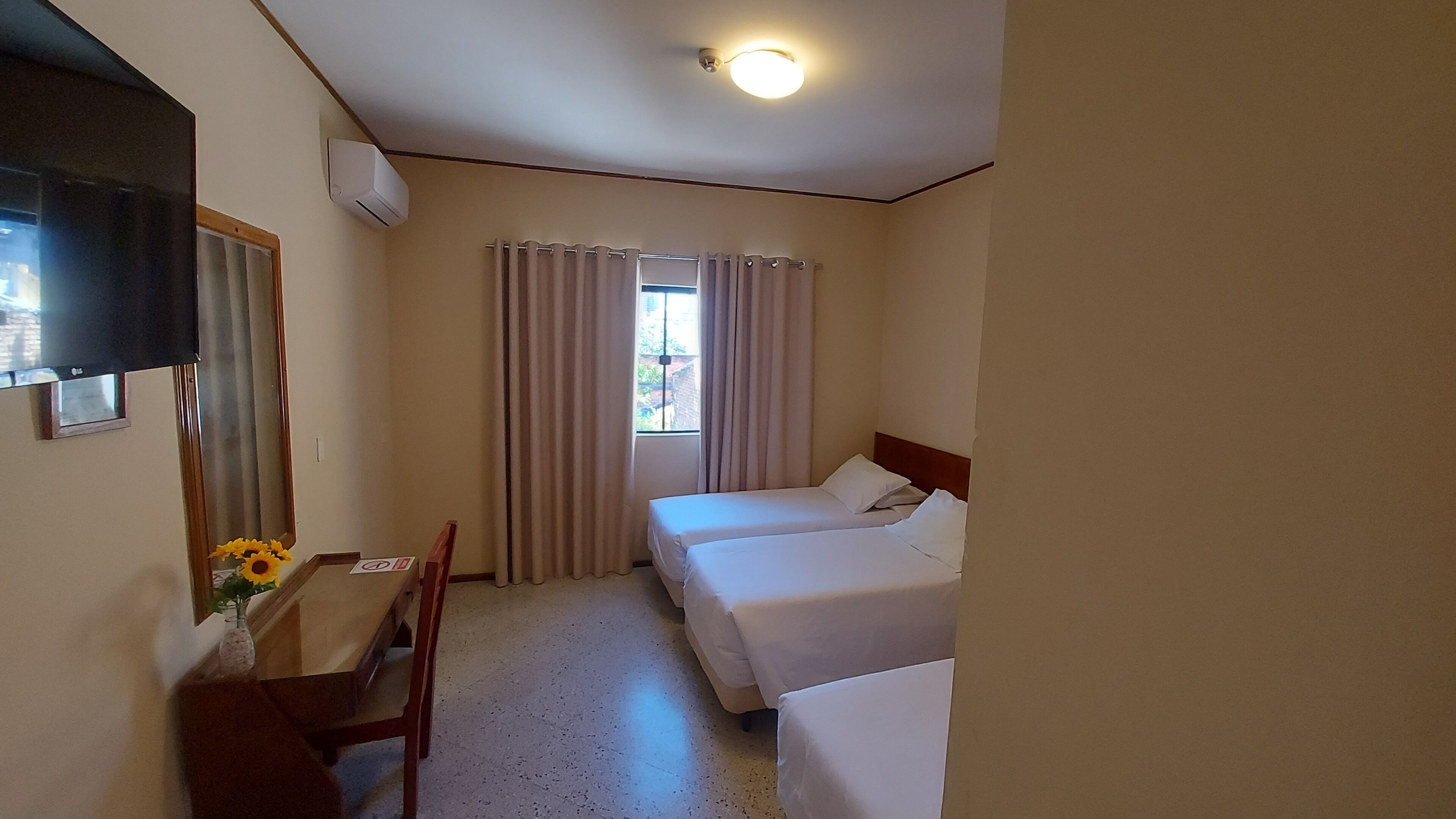 A hotel room with a bed, a desk, a chair, a TV, and a window with curtains.