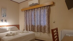A hotel room with a bed, a desk, a chair, an air conditioning unit, a window with patterned curtains, and a tiled floor. - Paranainn Hotel Asuncion (Asunción)