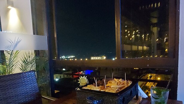 A dining table with pizzas and condiments, a window with a view of the city at night, and a potted plant. - Paranainn Hotel Asuncion (Asunción)
