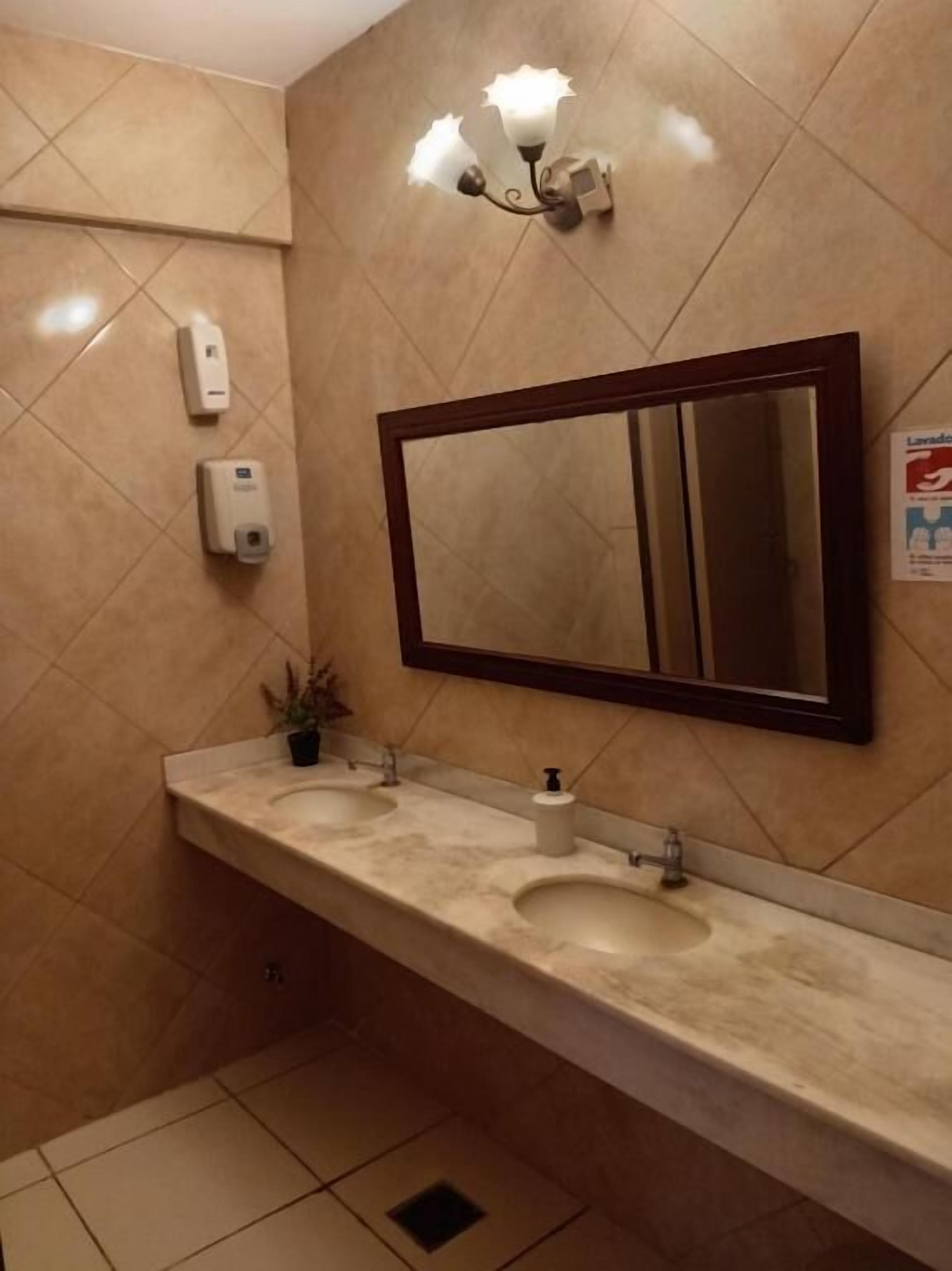 Une salle de bain équipée d’un lavabo double, d’un grand miroir et de deux distributeurs de solution hydroalcoolique.