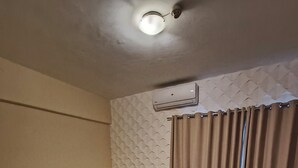 A hotel room with three single beds, a wooden headboard, an air conditioning unit, a curtain, and a small table with a chair. - Paranainn Hotel Asuncion (Asunción)