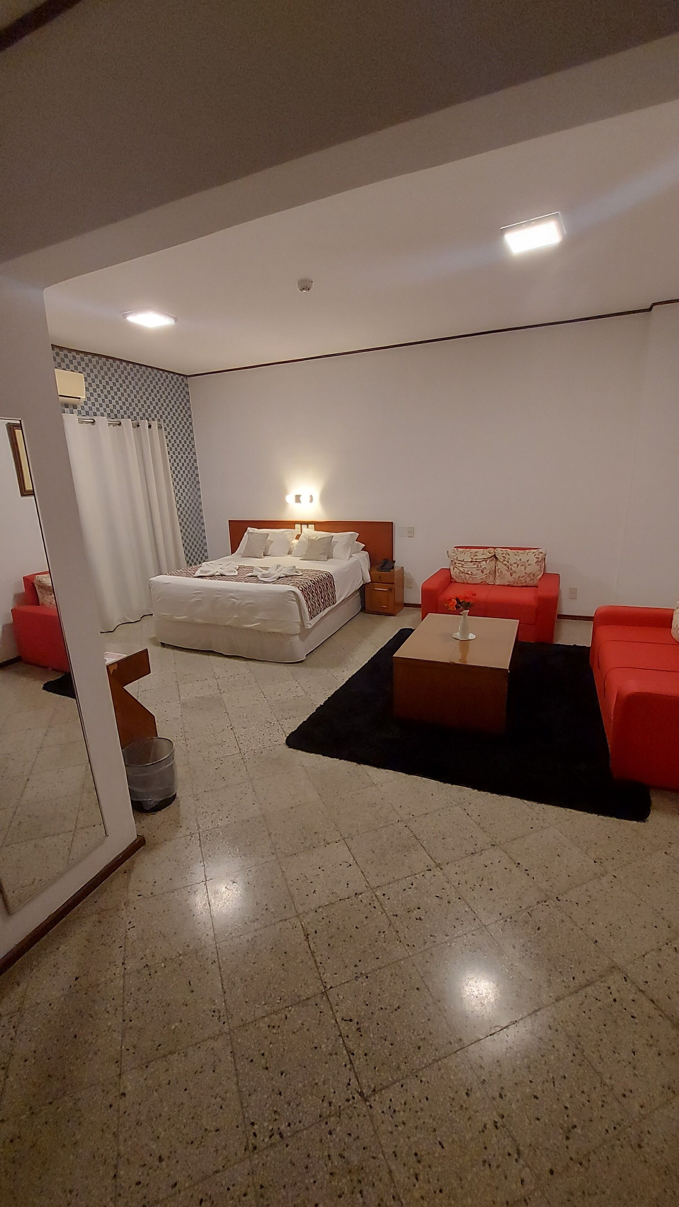 A modern hotel room with a bed, a red sofa, a small table, and a checkered wall pattern.