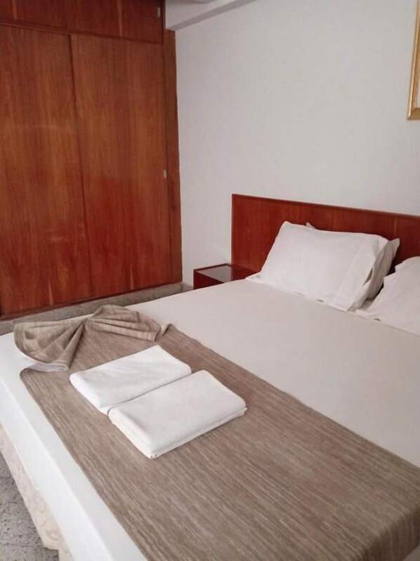 A neatly made bed with white linens, a wooden headboard, and a wooden wardrobe in the background.