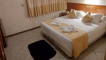 A hotel room with a bed, curtains, an air conditioner, a framed picture, and a telephone.