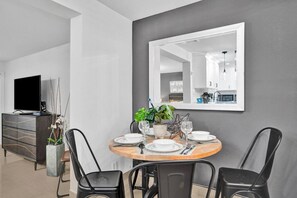 Un coin repas avec une table ronde, des chaises, un téléviseur et une cuisine en arrière-plan.