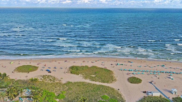 A beach with clear skies, calm sea, and beach umbrellas.