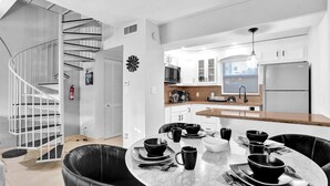 A modern kitchen with white cabinets, a central island, and a spiral staircase.