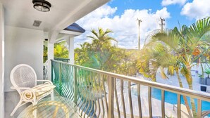 A balcony with a glass table and chairs, a pool, and tropical plants.