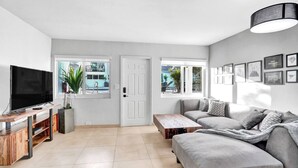 A living room with a TV, sofa, coffee table, and a door leading outside.