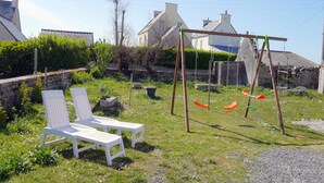 Viheralue, jossa on nurmikkoa, valkoisia lepotuoleja, keinuteline ja kiviseinät.