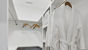 Un dressing accessible sans porte, avec un plancher en bois, des murs blancs et une robe suspendue.