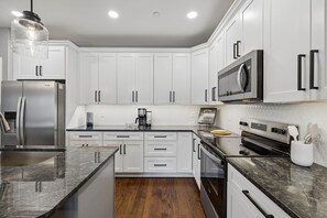 A modern kitchen with white cabinets, a stainless steel refrigerator, a microwave, and a stove.