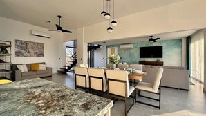 Een ruime woonkamer met een eettafel, stoelen, een bank, een televisie en een trap naar een hoger gelegen verdieping.