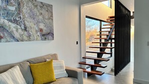 Een modern interieur met een grijze bank, abstracte kunst en een houten trap.