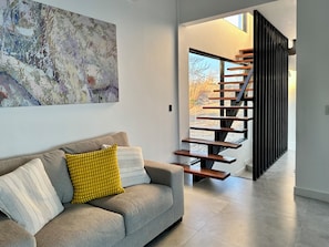 A modern interior with a grey sofa, abstract art, and a wooden staircase.