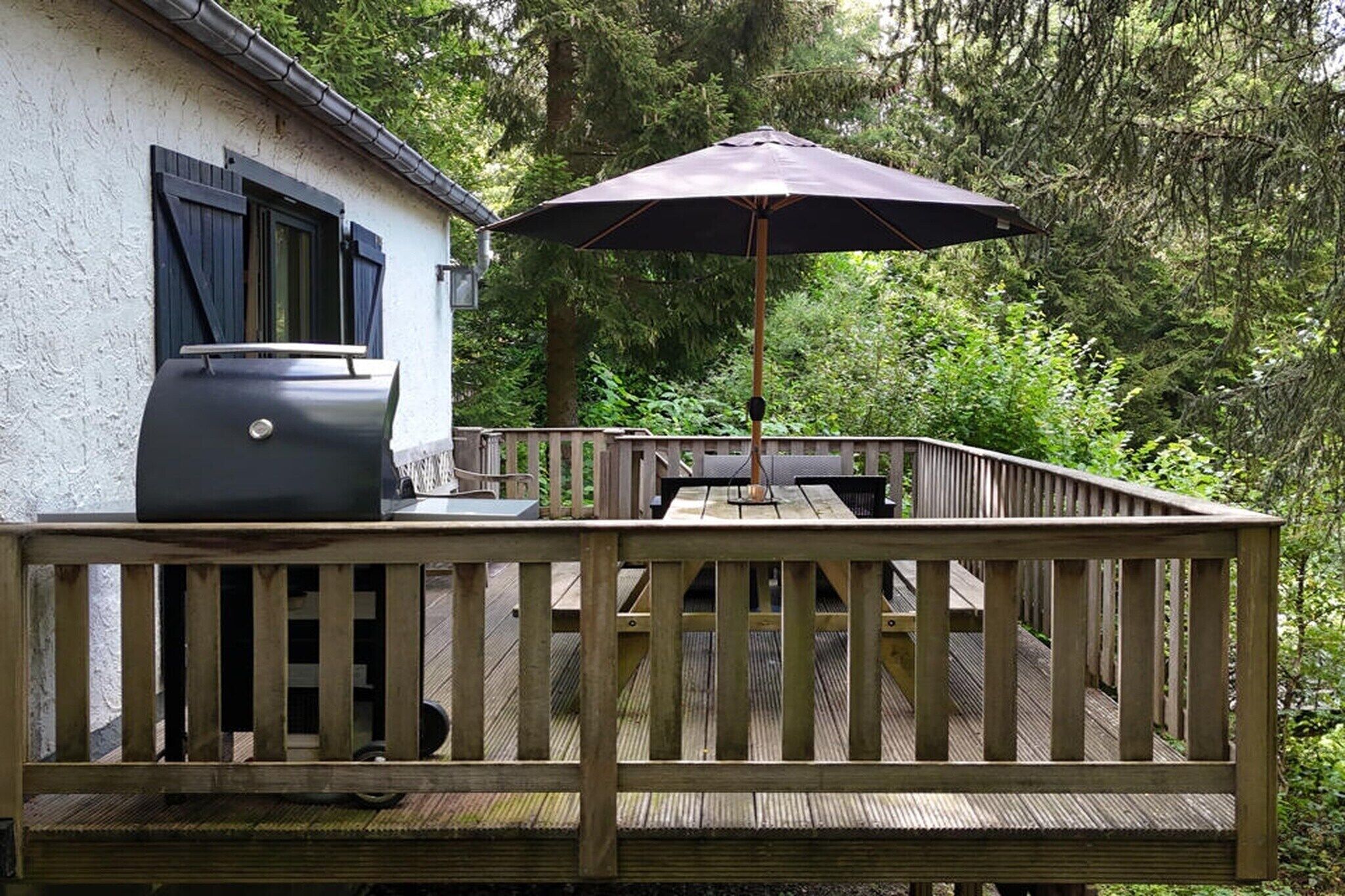 Eine Holzterrasse mit Grill und Sonnenschirm.