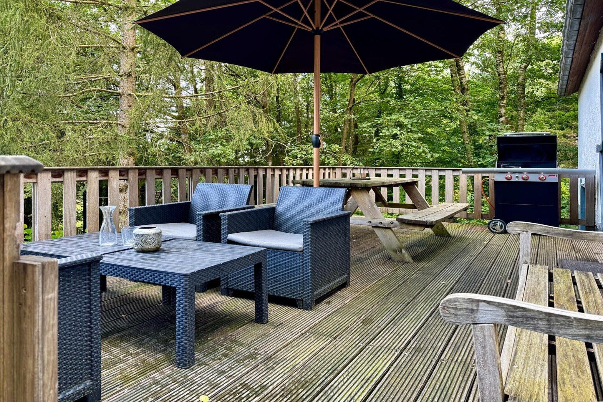Une terrasse extérieure aménagée avec des meubles en osier, un barbecue et un grand parasol.