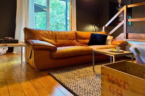 A room with a leather sofa, a small table, a wooden crate, and a window with a view of greenery.