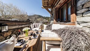 Un espacio para comer al aire libre con pared de piedra, muebles de madera y vistas a la montaña.