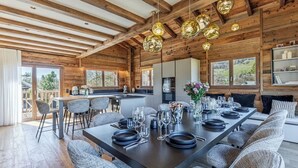 Interior moderno de una cabaña de troncos con comedor, cocina y ventanas amplias que ofrecen vistas al exterior.