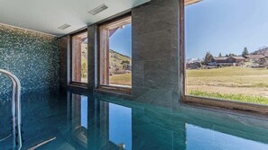 Ein moderner, überdachter Pool mit großen Fenstern, Steinwänden und freiem Blick auf die umliegende Landschaft.