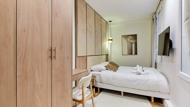 A bedroom with a bed, a desk, a chair, a wardrobe, a TV, and a painting on the wall. - Beautiful apartment with AC - Center of Paris (Paris)