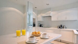 A modern kitchen with white cabinets, a breakfast table with croissants and coffee, and two glasses of orange juice. - Superb 2 bdr apartment Terrace Neuilly-sur-Seine (Neuilly-sur-Seine)
