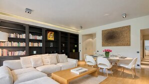 A modern living room with a sectional sofa, a wooden coffee table, a dining area with a white table and chairs, and a bookshelf filled with books. - Superb 2 bdr apartment Terrace Neuilly-sur-Seine (Neuilly-sur-Seine)