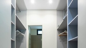 Un petit dressing étroit avec des étagères ouvertes, un sol carrelé et une porte donnant sur une salle de bain.