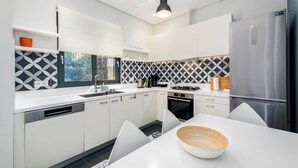 Une cuisine moderne avec des meubles blancs, un réfrigérateur en acier inoxydable, un four encastré et un coin repas comprenant une table et des chaises blanches.