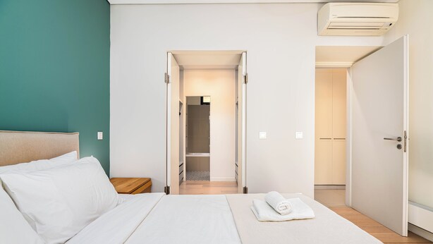 Une chambre d’hôtel avec un lit, une table de chevet, une salle de bain visible à travers une porte ouverte et une serviette sur le lit.