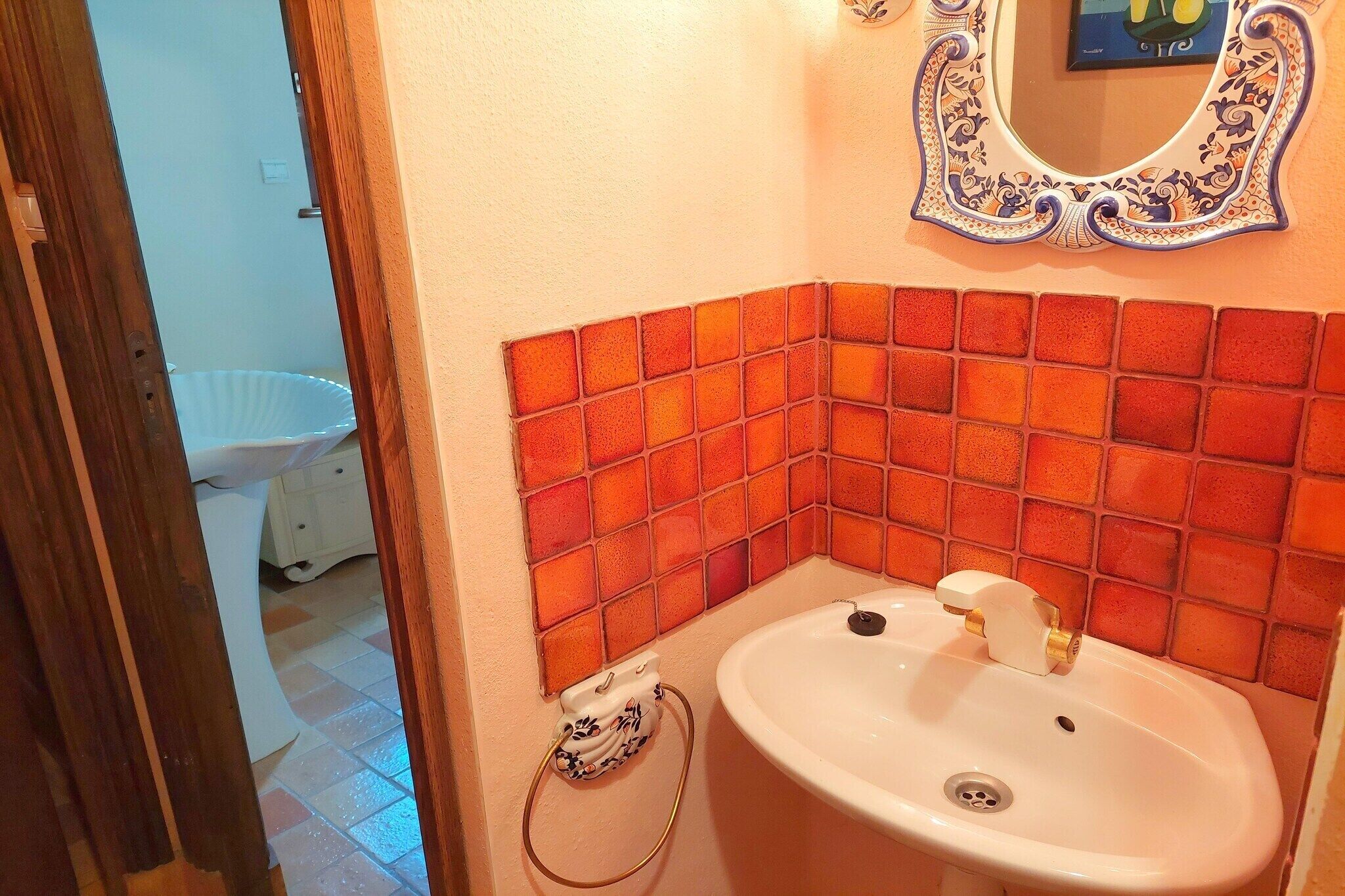 Une salle de bain avec un lavabo blanc, un miroir doté d’un cadre décoratif et un mur recouvert de carreaux.