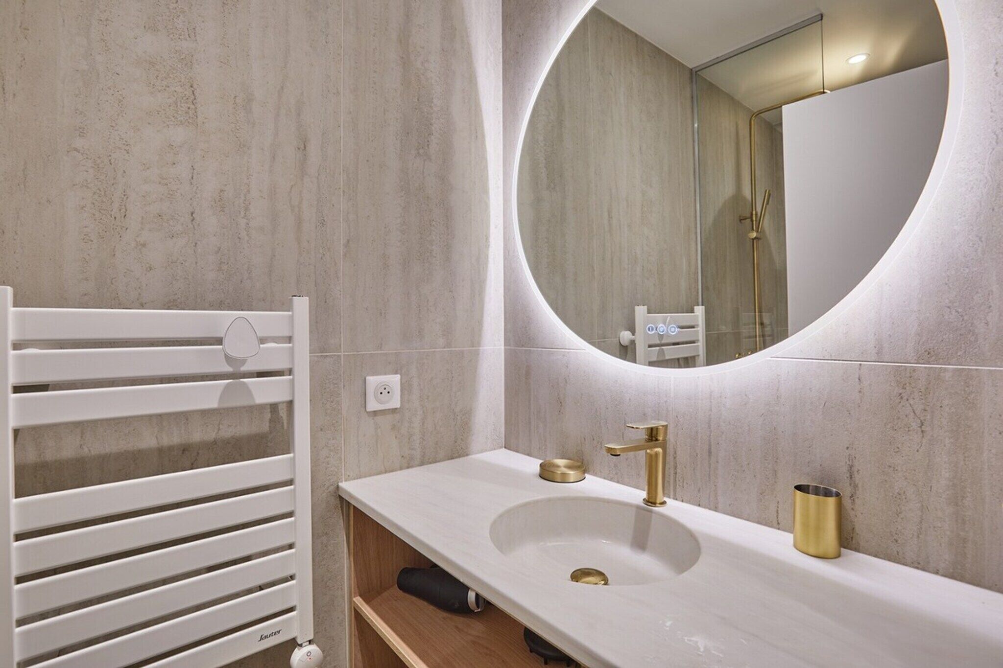 A bathroom with a white radiator, a sink with a gold faucet, and a round mirror.