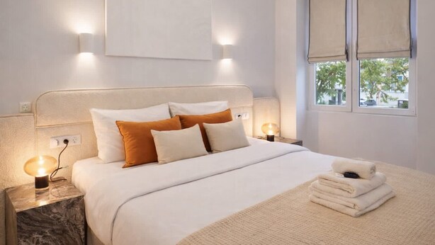 A neatly made bed with white and orange pillows, a bedside lamp, and a window with curtains. - Beautiful renovated apartment with AC - Paris East (Paris)