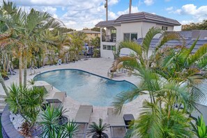 A swimming pool surrounded by palm trees and a modern building with a flat roof. - Stylish 1BR Suite w/ Pool & Steps to the Beach (Pompano Beach)