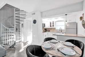 Una cocina moderna con armarios blancos, microondas integrado y refrigerador de acero inoxidable.