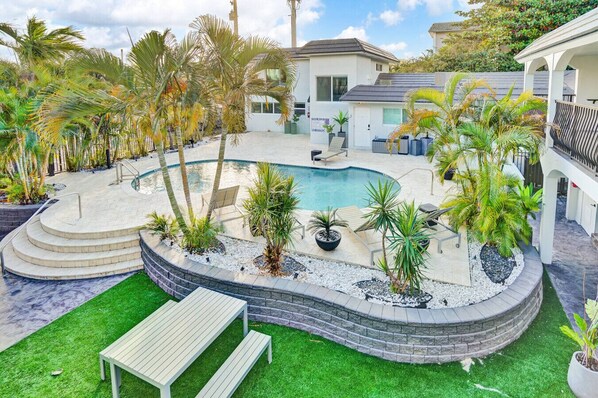 A swimming pool with a curved design, surrounded by palm trees and a stone deck. - Stylish 1BR Suite w/ Pool & Steps to the Beach (Pompano Beach)