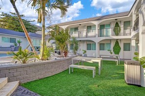 A multi-story hotel with outdoor seating, palm trees, and a pool. - Stylish 1BR Suite w/ Pool & Steps to the Beach (Pompano Beach)