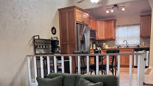 A living room with a green sofa, a coffee table, and a view of a kitchen with wooden cabinets and a dining area. - The Sunset Perch | Pet-Friendly + Deck (Eureka Springs)