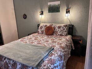 Ein Bett mit floraler Bettwäsche, zwei Wandlampen, ein kleiner Tisch und ein Bild an der Wand.