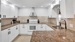 A modern kitchen with white cabinets, a stainless steel range hood, granite countertops, and a built-in oven. - Modern Beachside 2BR | Steps to Beach + Heated Pool (Pompano Beach)